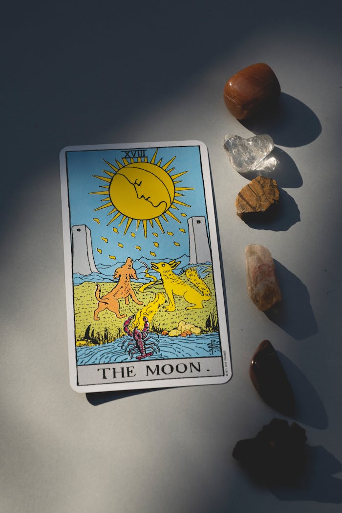 A tarot card depicting the moon with healing crystals arranged beside it, capturing light and shadow.